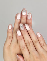 Hand wearing Naillover Beige Elegance handmade press on nails with shimmering cat eye finish, silver butterfly charms, and glitter stripe details.